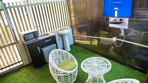 Een compacte keuken met een koelkast, spoelbak en een klein eethoekje met twee rieten stoelen.