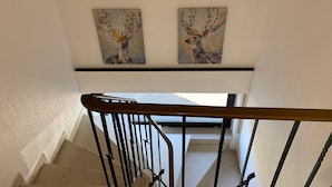 Una escalera con barandilla de metal, paredes color beige y dos cuadros con ciervos en la pared.