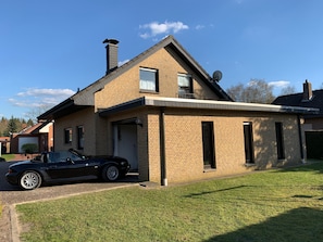 A two-story house with a brick exterior, a satellite dish, and a black car parked in the driveway. - Holiday Home "Wacholderhain" Near the Lake with Garden (Haselünne)