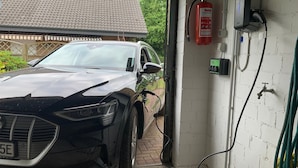 Un coche negro estacionado en un garaje con un extintor de incendios colgado en la pared, una estación de carga para bicicletas y un grifo.