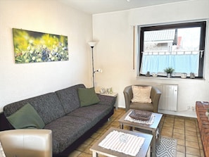 A living room with a sofa, armchair, coffee table, and a painting on the wall. - Holiday Home "Wacholderhain" Near the Lake with Garden (Haselünne)