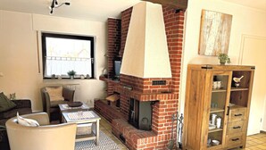 Una sala de estar con chimenea de ladrillo, un mueble de madera, un sofá, una mesa de centro y una ventana con vistas.