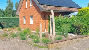 A brick house with a sloped roof, solar panels, and a garden with various plants. - Holiday Home by the Lake with Garden and Terrace (Haselünne)