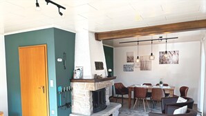 A living room with a fireplace, dining area, and a door. - Holiday Home by the Lake with Garden and Terrace (Haselünne)