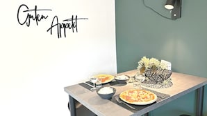 A dining table with two pizzas, bowls, and glasses, a decorative vase, and a wall-mounted light fixture. - Holiday Home by the Lake with Garden and Terrace (Haselünne)
