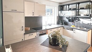 A modern kitchen with a central island, built-in appliances, and a window providing natural light. - Holiday Home by the Lake with Garden and Terrace (Haselünne)