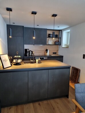 A modern kitchen with dark cabinetry, pendant lighting, a central island, and a coffee station.