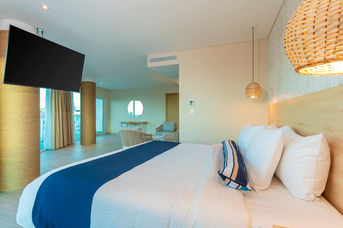 Une chambre d’hôtel moderne dotée d’un grand lit, d’un téléviseur à écran plat, de lampes en osier et offrant une vue sur le balcon et l’espace repas.