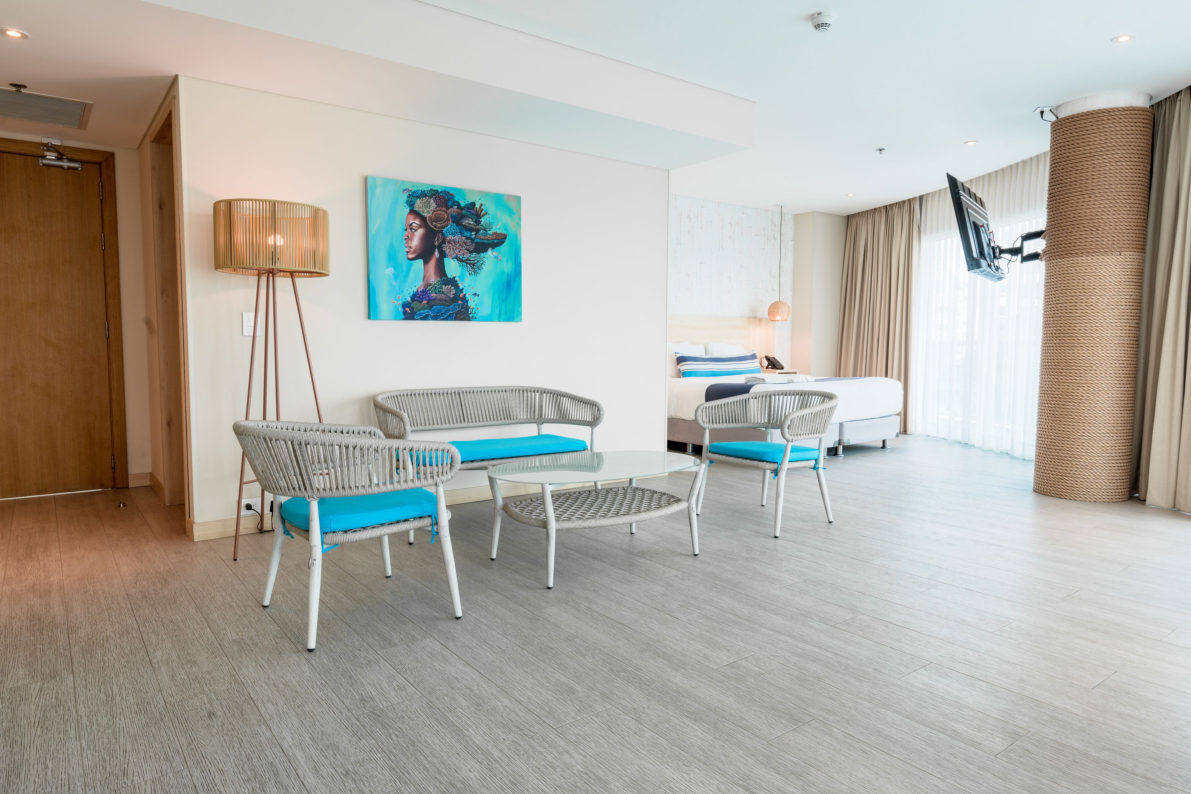 Una sala de estar moderna con muebles de mimbre, un cuadro grande y un televisor fijado a un pilar.