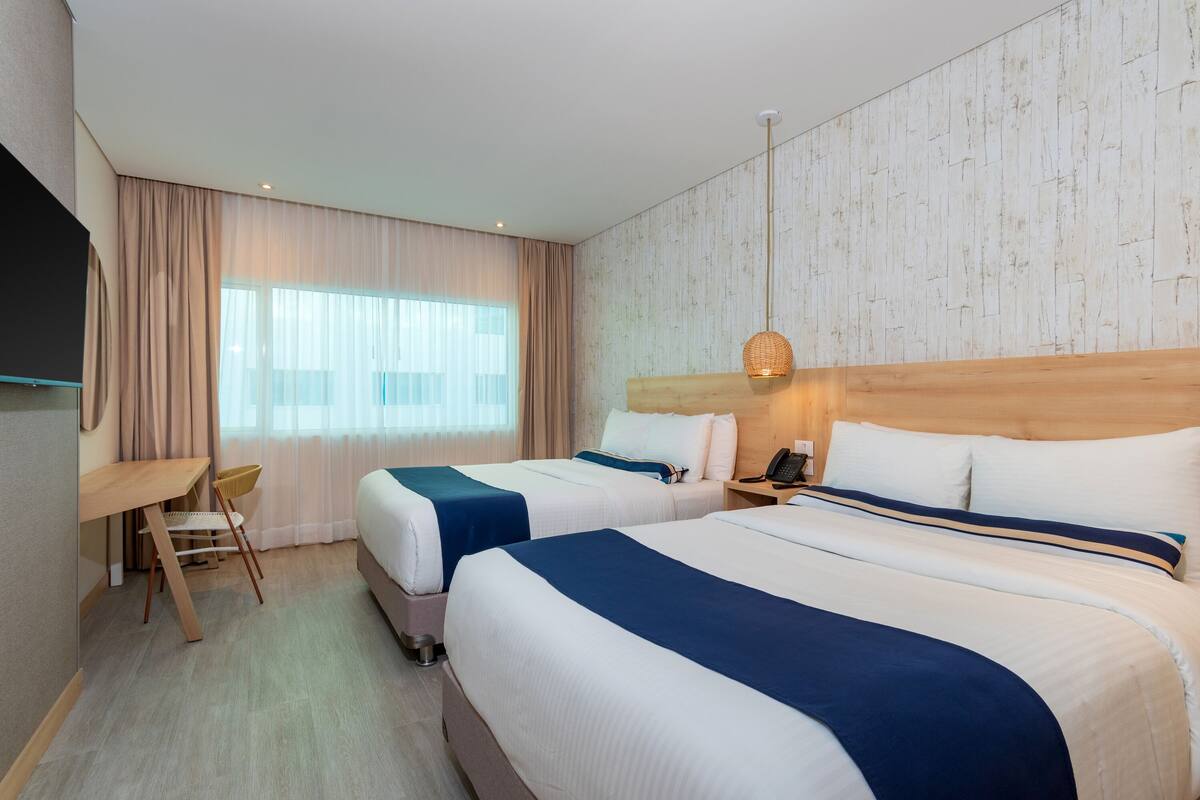 Une chambre d’hôtel avec deux lits, un bureau, une chaise et une grande fenêtre avec des rideaux.