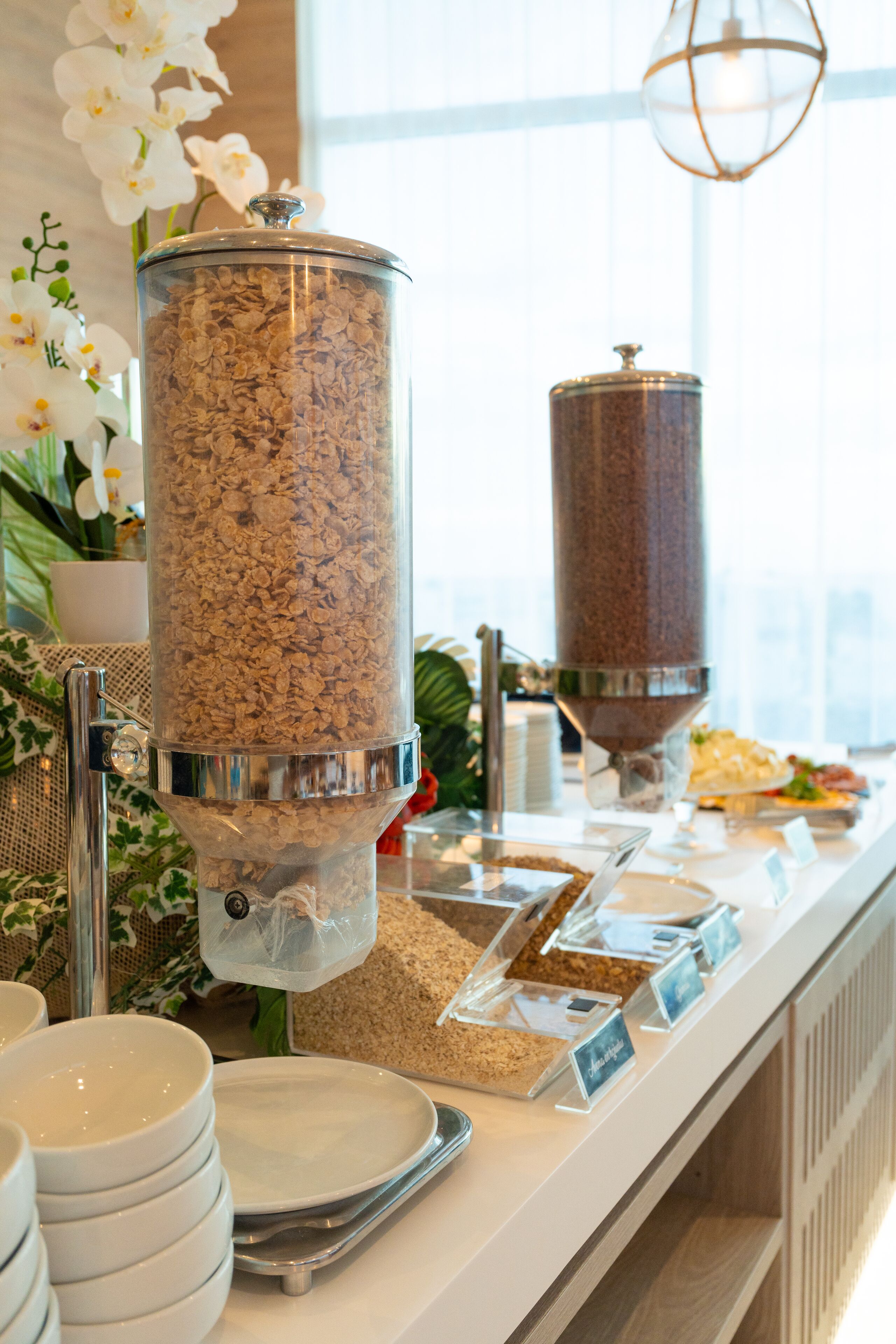 Disposición de bufé con dispensador de granola, tazones y un cartel que indica 'Cereal Bar'.
