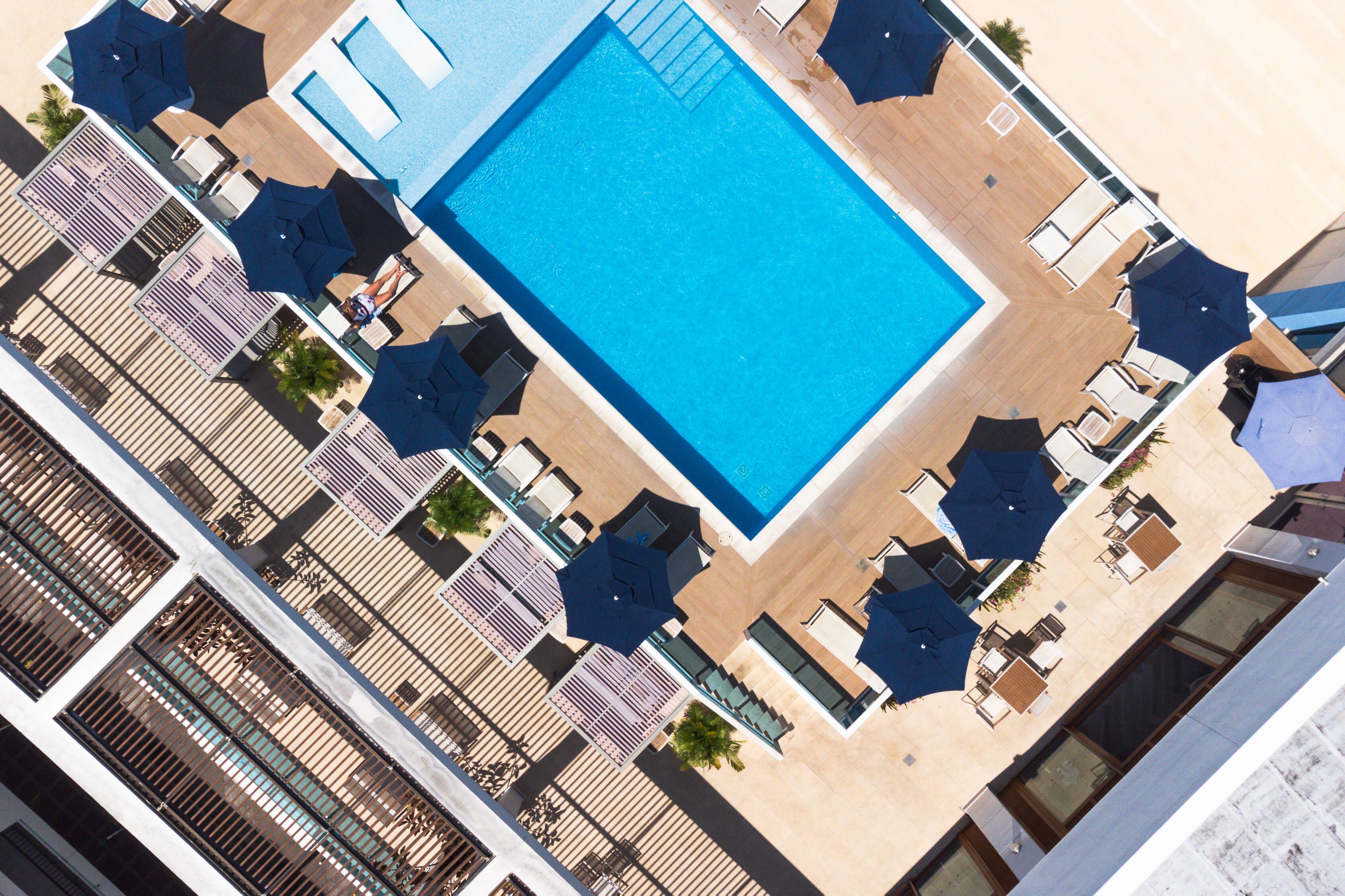 Vista aérea de un hotel con piscina, rodeado de tumbonas y sombrillas.
