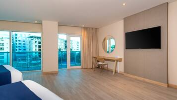 Habitación de hotel con una cama grande, un escritorio, una silla, un televisor y vista a la ciudad por la ventana.