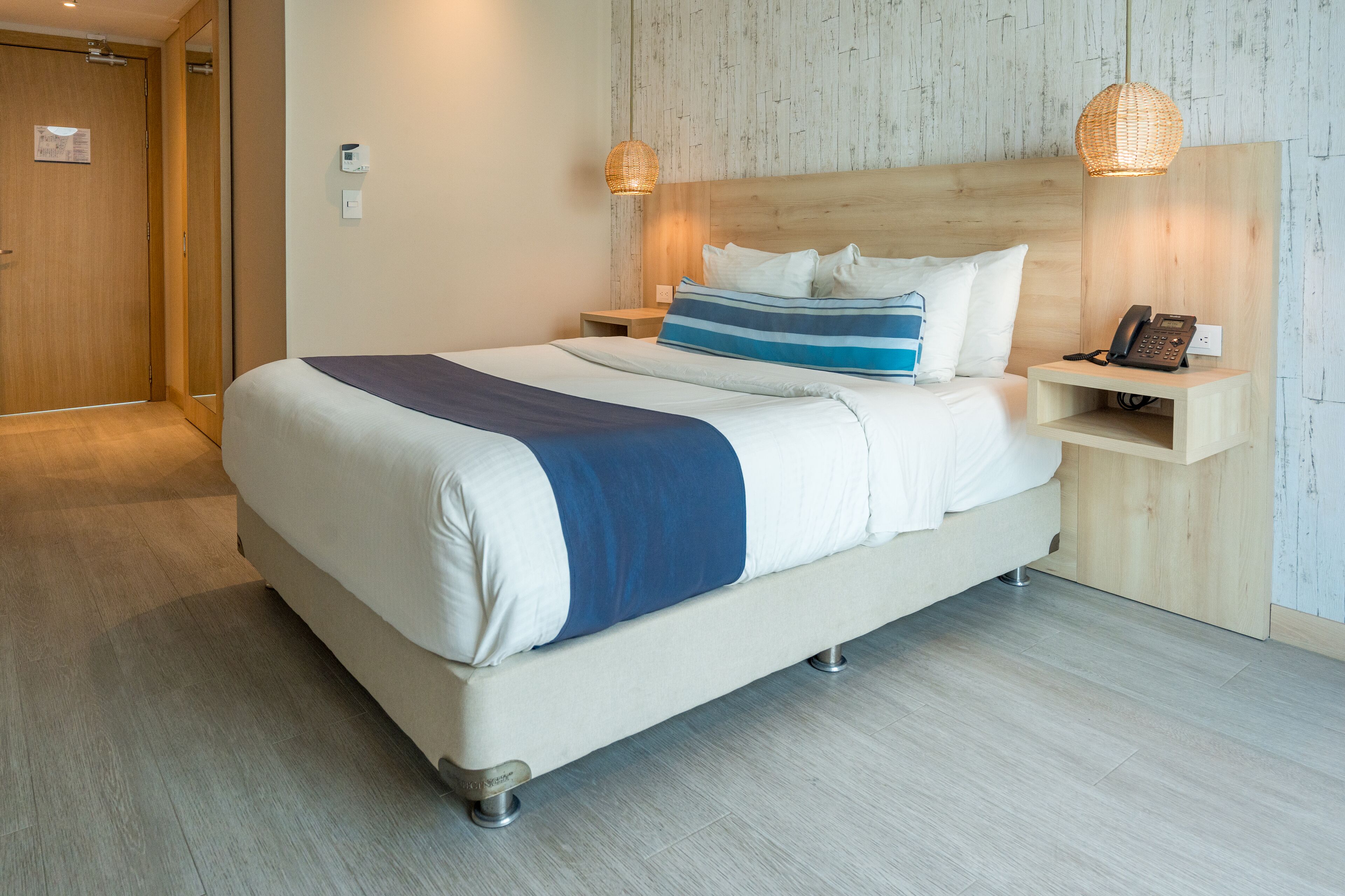 Ein modernes Hotelzimmer mit einem großen Bett, Nachttischen, einem Holz-Kopfteil und einer hellen Wand mit strukturierter Oberfläche.