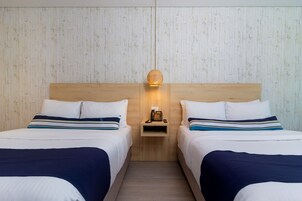 Habitación de hotel con dos camas, cabecero de madera, mesita de noche pequeña con lámpara y teléfono.