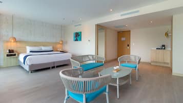Quarto de hotel com cama, duas cadeiras de vime com almofadas azuis, uma mesa redonda pequena, um armário de madeira e uma porta que dá para outro cômodo.