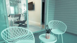 Una habitación moderna con dos sillas blancas y una mesita, un televisor montado en la pared, y vistas a través de un ventanal.