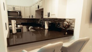 Una cocina moderna con armarios blancos, encimera oscura y una isla central con taburetes de bar.