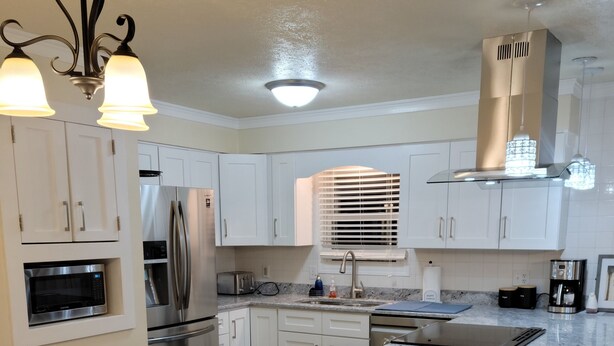 Una cocina moderna con armarios blancos, electrodomésticos de acero inoxidable, una isla central con taburetes y una mesa de comedor.