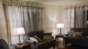 Una sala de estar con dos sofás, una mesa de centro, una mesita auxiliar con una lámpara y una alfombra estampada.