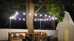 Una terraza al aire libre con una mesa y sillas de madera, rodeada por una valla blanca y un árbol.