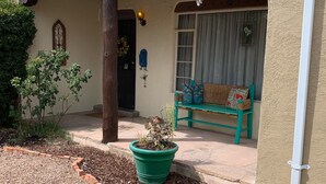 A covered patio area with a green bench, a potted plant, and a small garden with yellow flowers. - Casa Bonita located 2 blocks from Old Town  (Albuquerque)