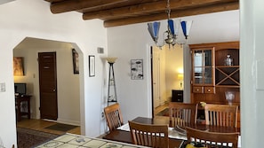 Un comedor con mesa y sillas de madera, una araña y un aparador con cristalería.