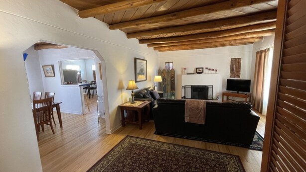A living room with a black sofa, wooden floor, and a TV. There is a dining area with chairs and a table. - Casa Bonita located 2 blocks from Old Town  (Albuquerque)