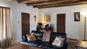 A living room with a black leather sofa, two patterned throw pillows, a wooden coffee table, a lamp, a TV, and a small side table with a radio. - Casa Bonita located 2 blocks from Old Town  (Albuquerque)