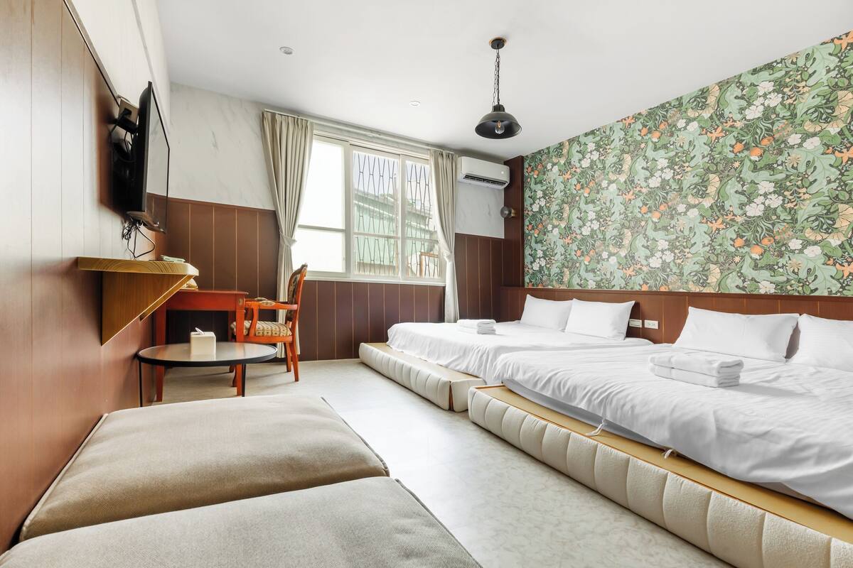 A hotel room with two beds, a small table, a chair, and a TV mounted on the wall.