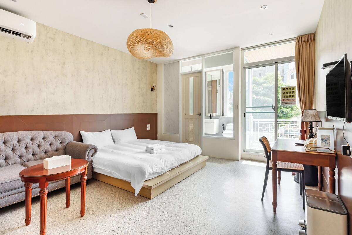 A hotel room with a bed, a sofa, a dining table, and a TV.