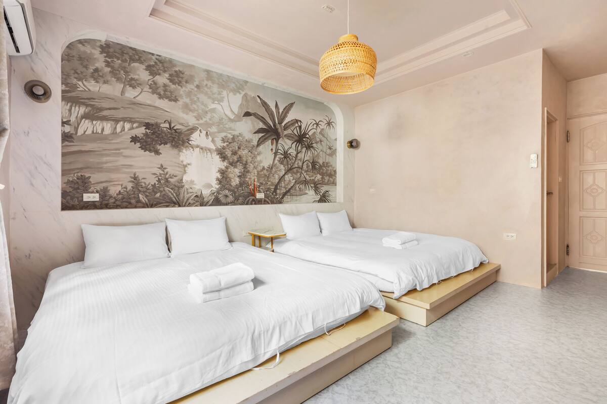 A bedroom with two beds, a mural on the wall, and a hanging light fixture.