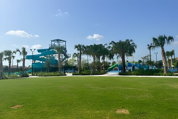 Un parc doté d’une vaste pelouse verdoyante, de palmiers et d’une structure de toboggan aquatique.