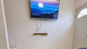 Puinen sohvapöytä, jossa on sisäänrakennettu hylly, seinälle asennettu taulutelevisio ja taustalla näkyvä ovi.