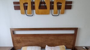 Siististi pedattu sänky, jossa on raidallinen vuodevaatteisto, puinen pääty ja seinälle kiinnitetty koriste-esine päädyn yläpuolella.