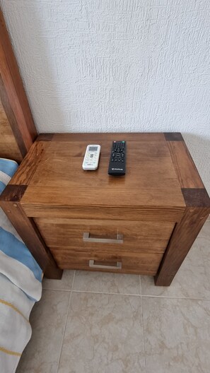 A wooden bedside table with two remote controls and a drawer. - Cookie House Cancun Mex (Cancun)