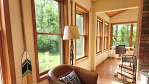 Une pièce chaleureuse avec un fauteuil en cuir, une lampe et de grandes fenêtres donnant sur l’extérieur.