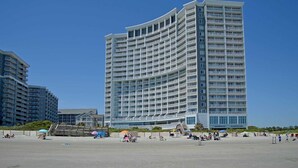 Ein Hochhaus-Hotel mit mehreren Balkonen, in Strandnähe, mit Personen und Sonnenschirmen.