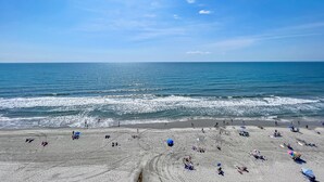 Ein Strand mit badenden und sonnenden Personen und einem klaren, blauen Himmel.