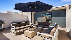 A modern outdoor seating area with a fire pit, white furniture, and a large umbrella.