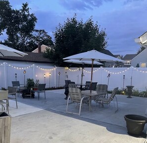 An outdoor patio with a table and chairs, string lights, and umbrellas.