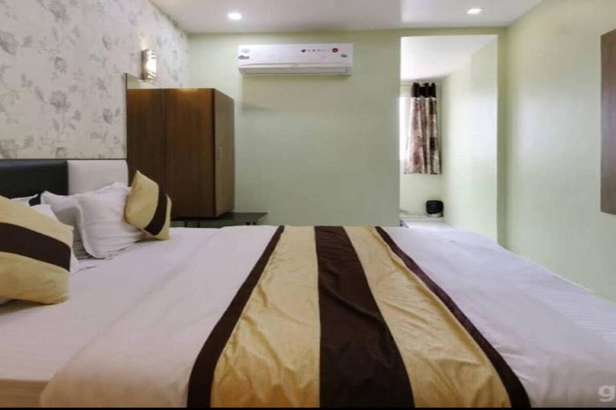 A hotel room with a bed, a wardrobe, an air conditioning unit, and a curtain.