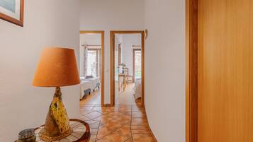 Een gang met een lamp, een houten deur en een glimp van een kamer met een bed en een raam.