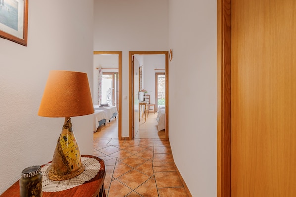 A hallway with a lamp, a wooden door, and a glimpse of a room with a bed and a window. - Vacation Home Castle House with A/C, Terrace & Garden (Redondo- Alentejo)