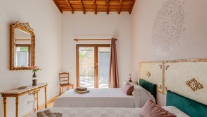 Une chambre avec deux lits, un plafond en bois, un grand miroir, une fenêtre avec des rideaux et un mur à motifs.