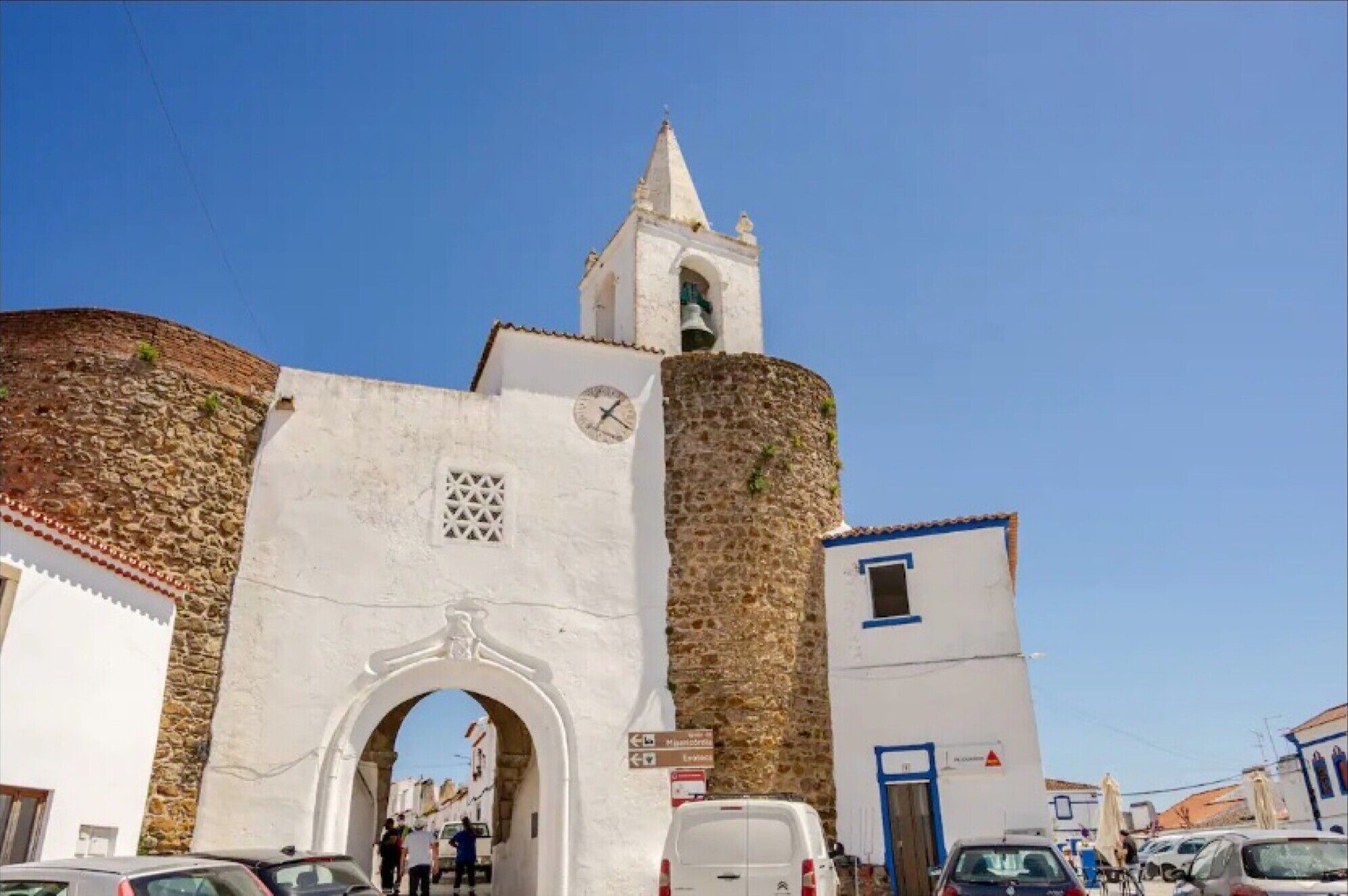 A historic building with a clock tower, an archway entrance, and a sign indicating directions.