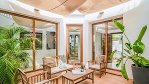 Un patio soleado con mobiliario de madera, ventanas amplias y plantas en macetas.