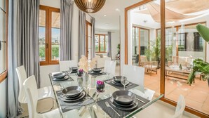 Un comedor con mesa de vidrio, sillas blancas y vistas al patio exterior.