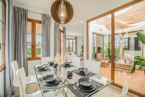 A dining area with a glass table, white chairs, and a view of the outdoor patio.