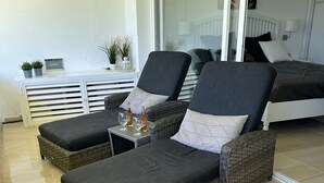 Un balcón con dos sillones de mimbre, una mesita con bebidas y un mueble consola blanco con plantas.
